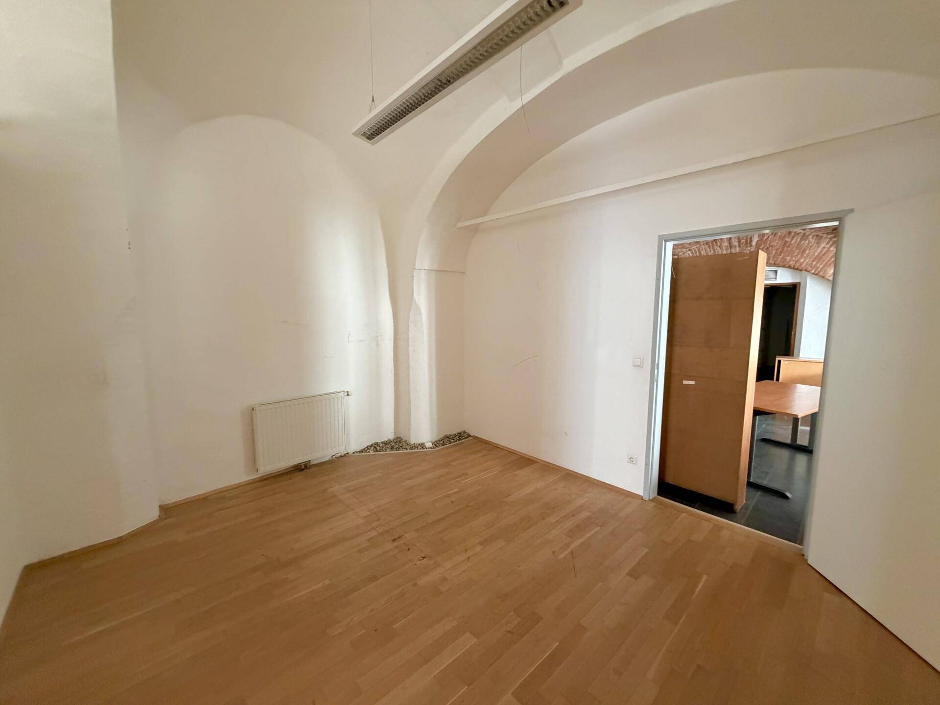 Leeres Büro mit gewölbter Decke, Holzboden und einem Heizkörper unter dem Fenster.