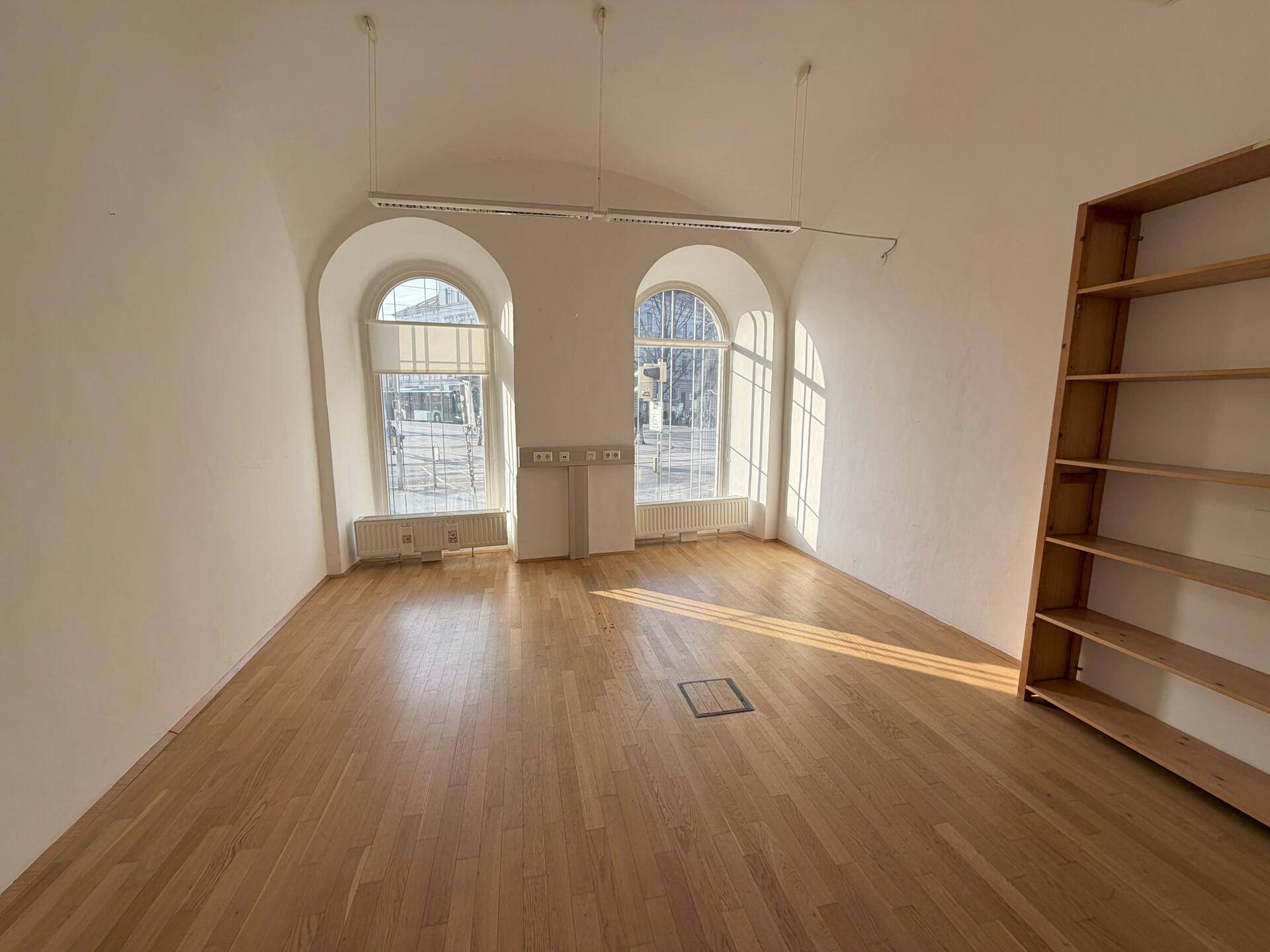 Geräumiges, leeres Büro mit gewölbter Decke, Holzboden und zwei großen Rundbogenfenstern.