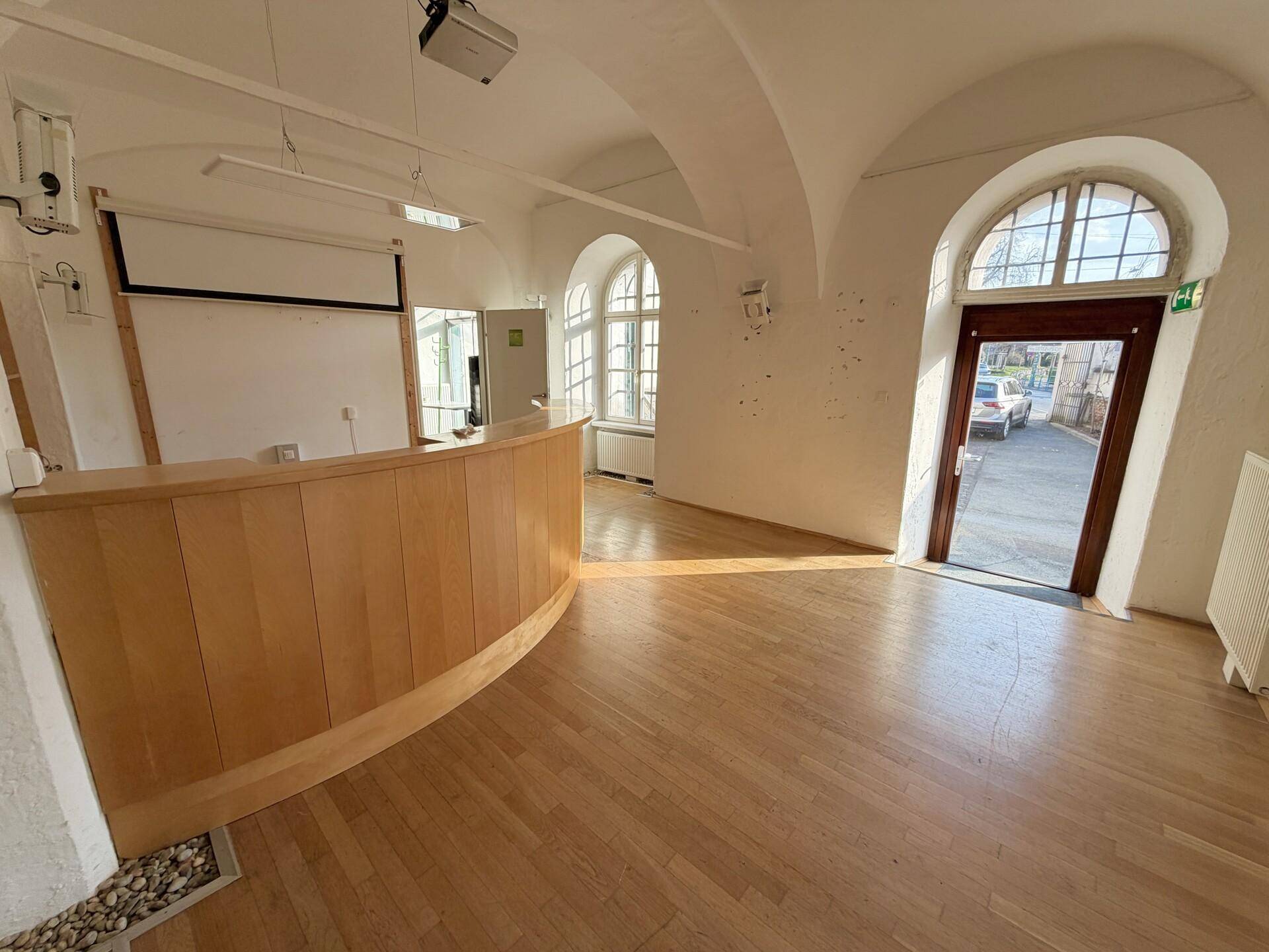 Heller Empfangsbereich mit gewölbter Decke, Holzboden und großen Rundbogenfenstern.