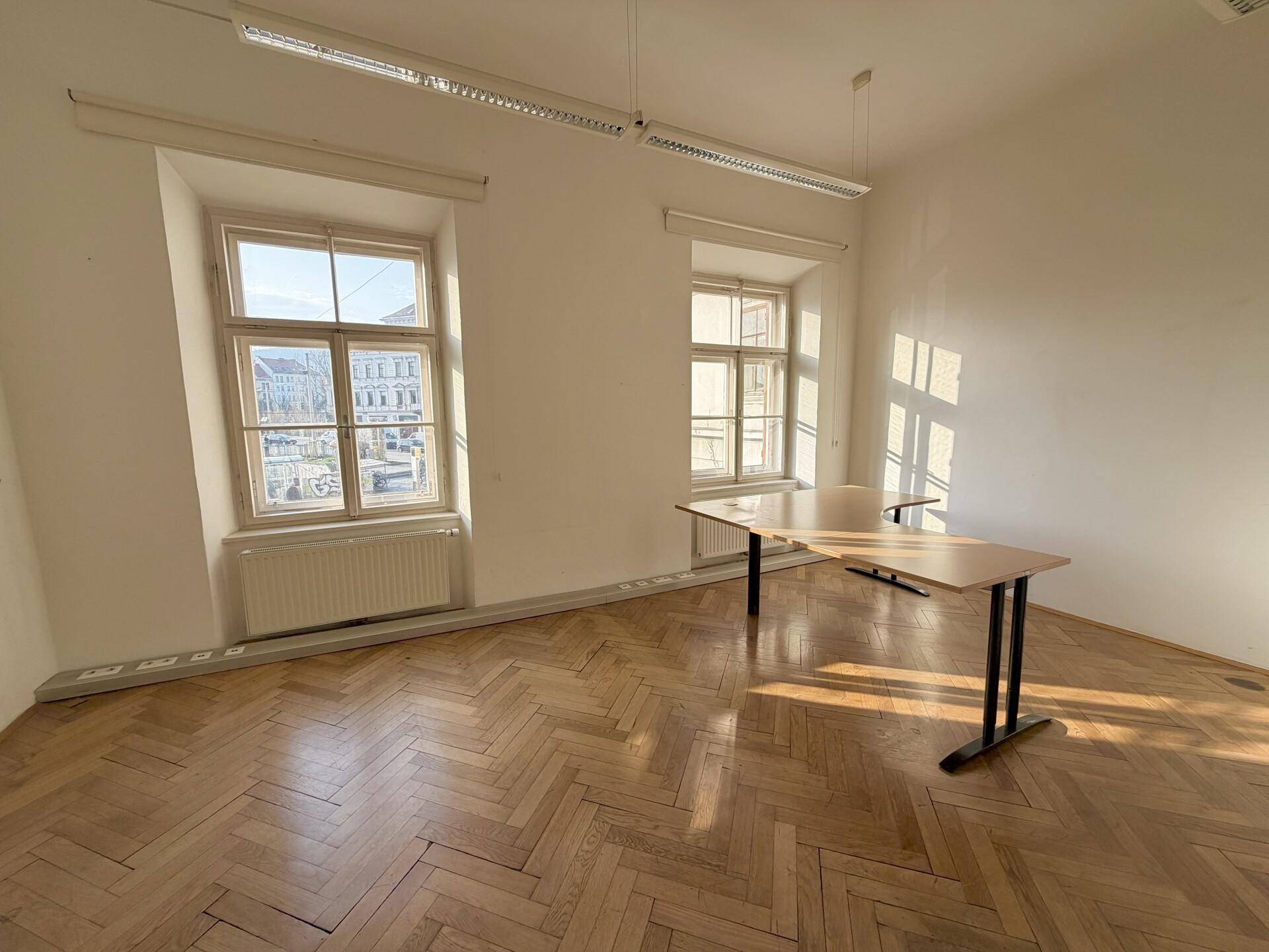Geräumiges Büro mit Fischgrätparkett, zwei großen Fenstern und reichlich natürlichem Tageslicht.