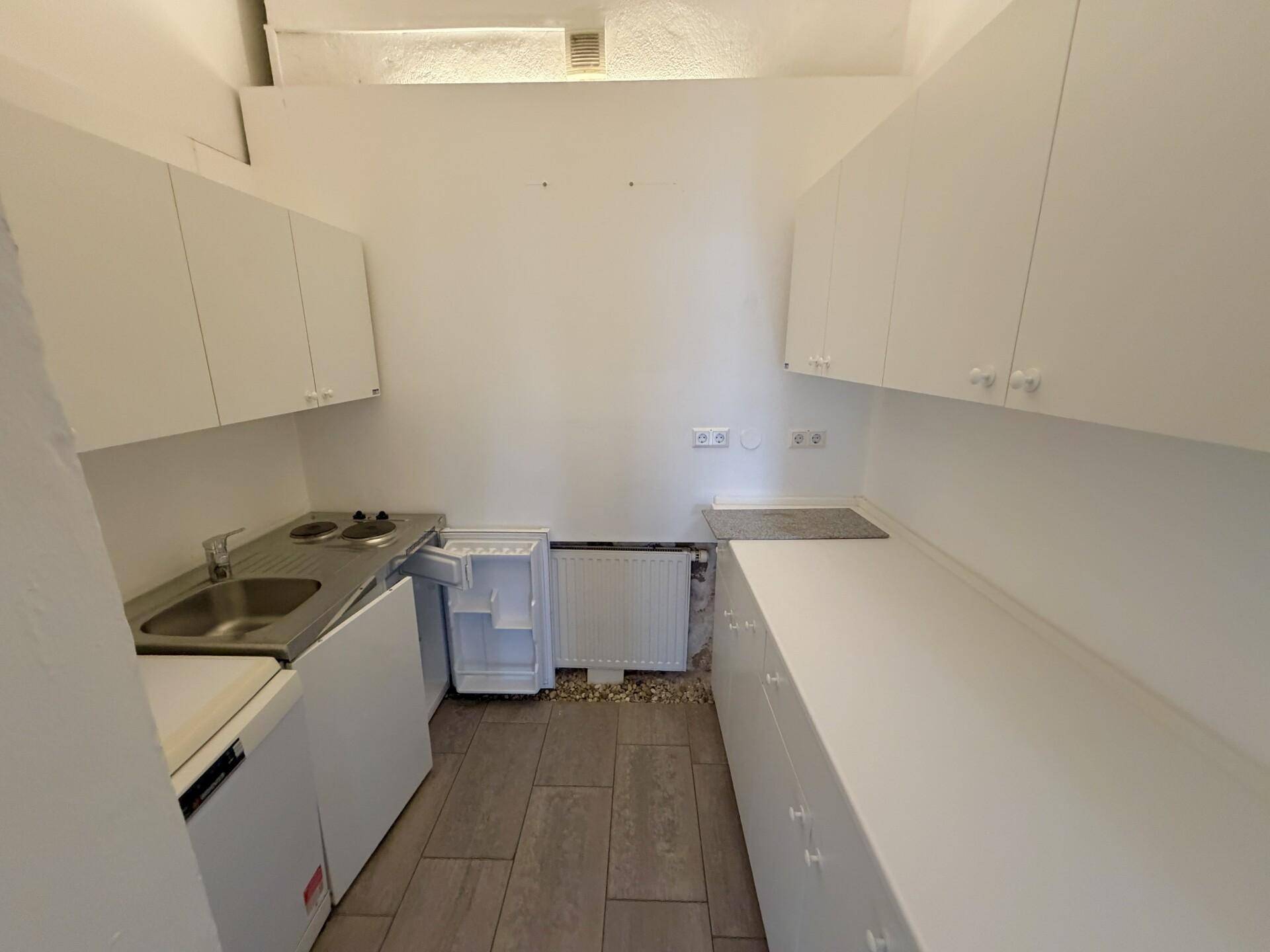 Funktionale Küchenzeile mit weißen Schränken, Spüle, Kochfeld und einem kleinen Kühlschrank.