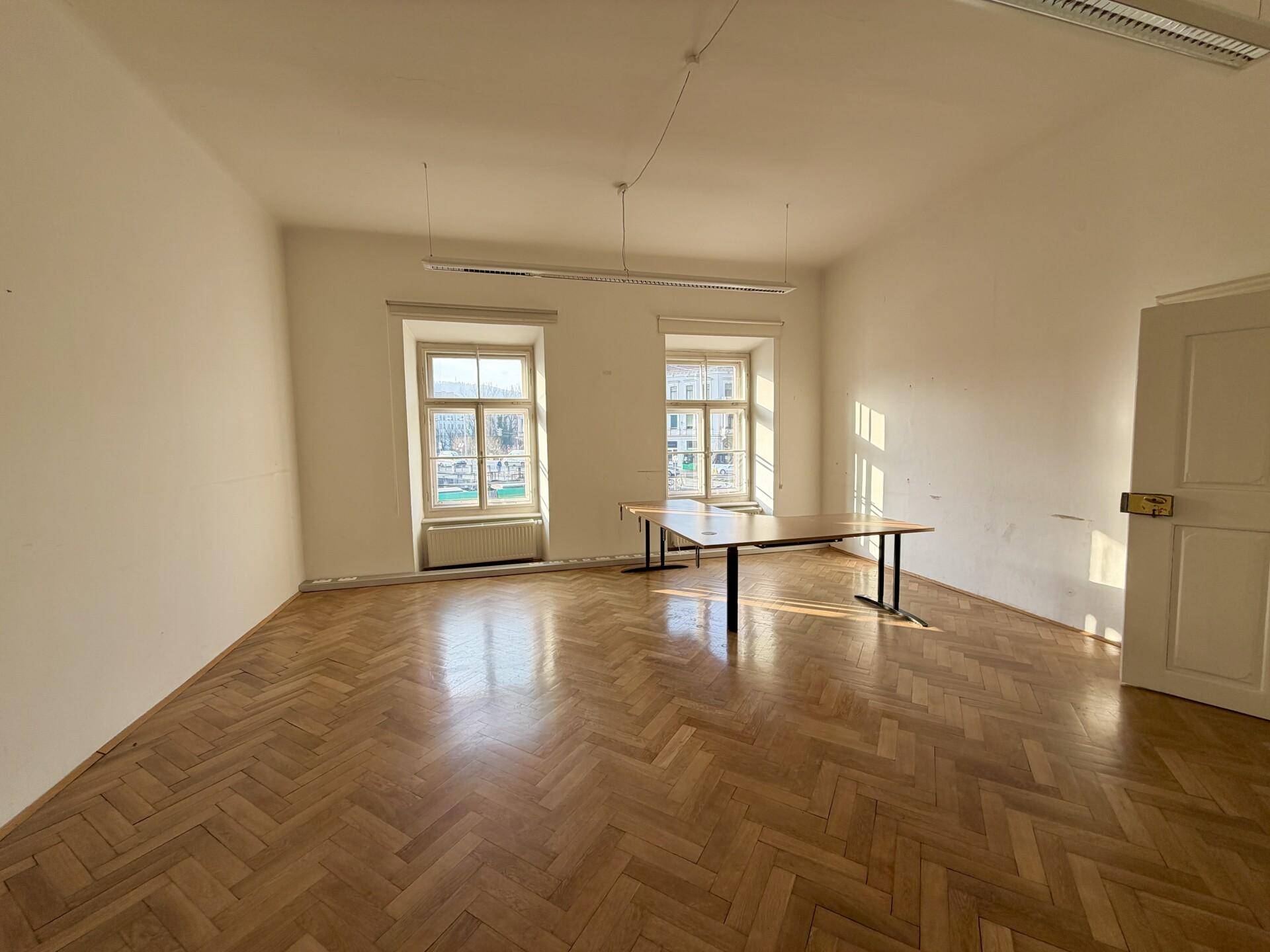 Geräumiges Büro mit Fischgrätparkett, zwei Fenstern und reichlich natürlichem Licht.