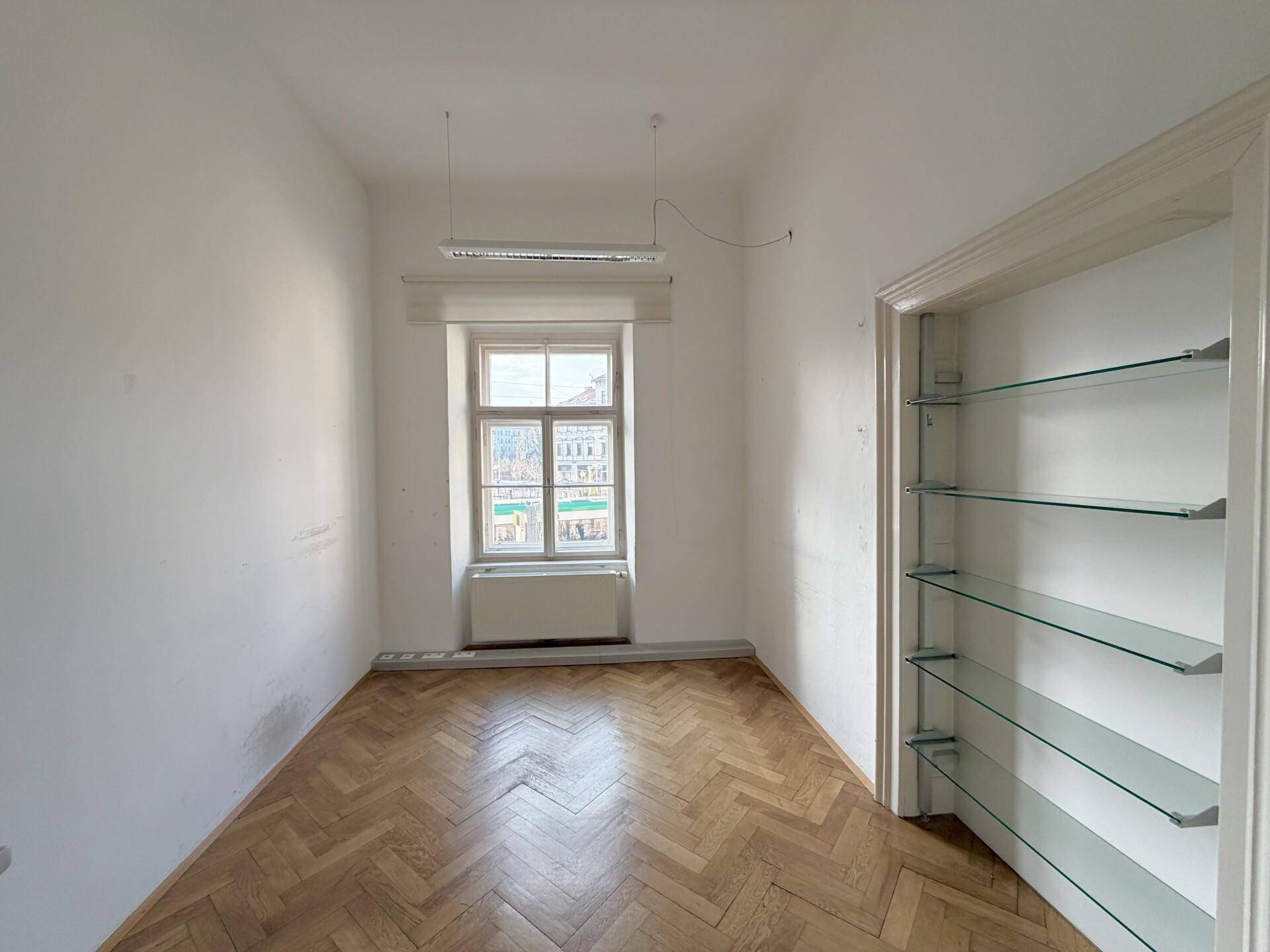 Helles Einzelbüro mit Fischgrätparkett, einem Fenster und praktischen eingebauten Regalen.