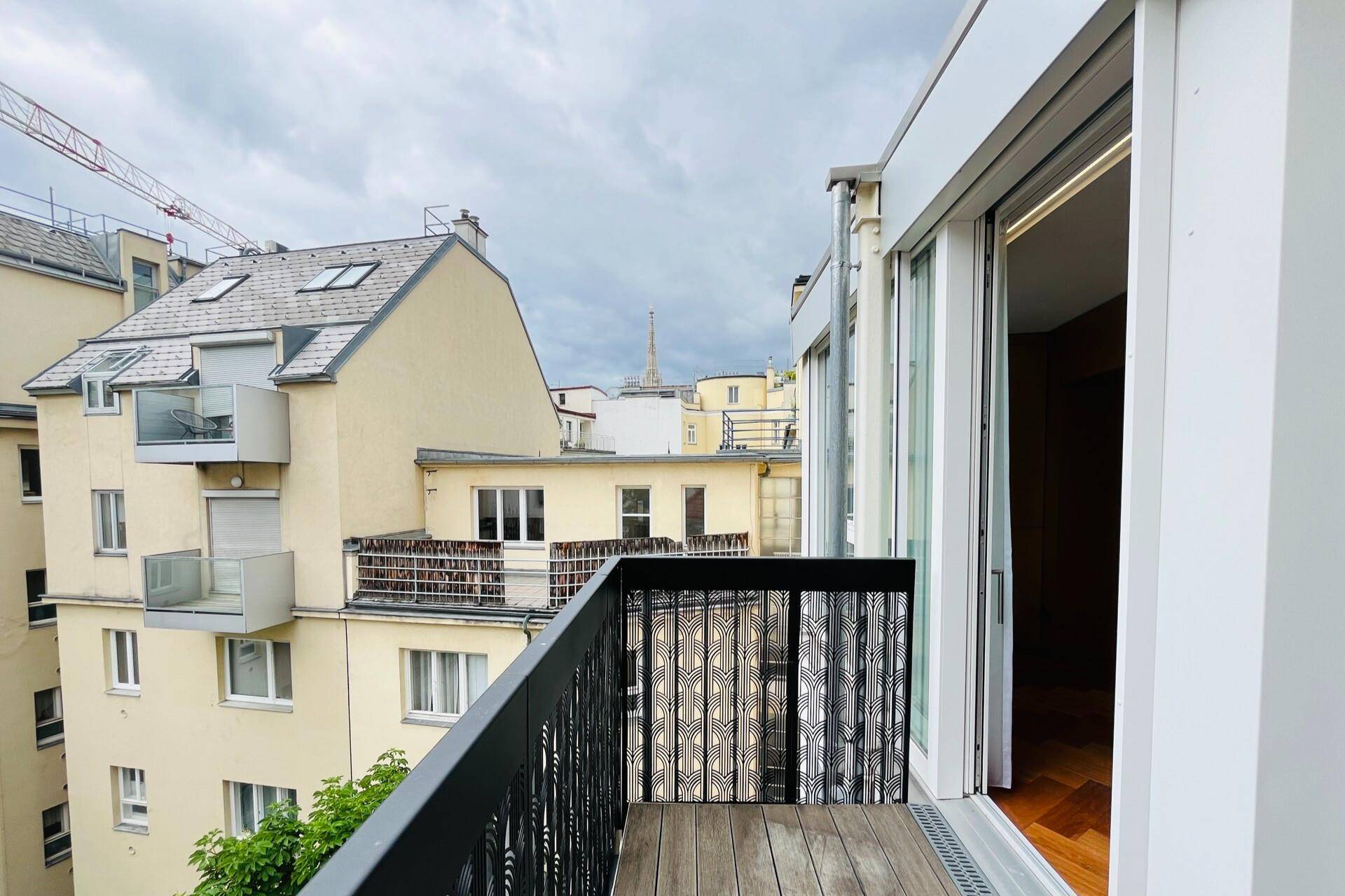 Balkon mit Holzboden und Blick auf die umliegende Stadtarchitektur und einen Kirchturm.