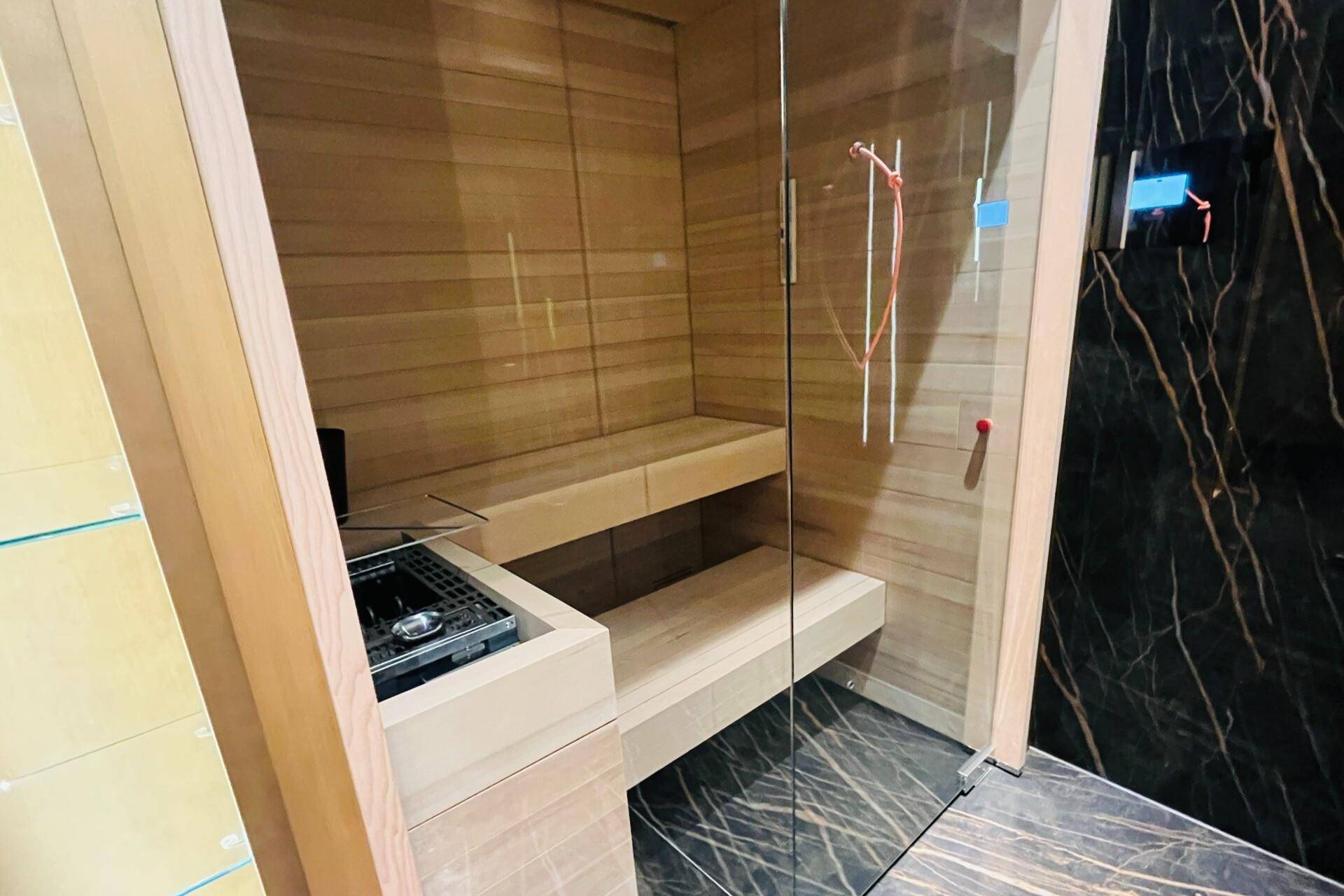 Moderne Sauna mit Holzausstattung und Glastür, integriert in einen luxuriösen Bereich.