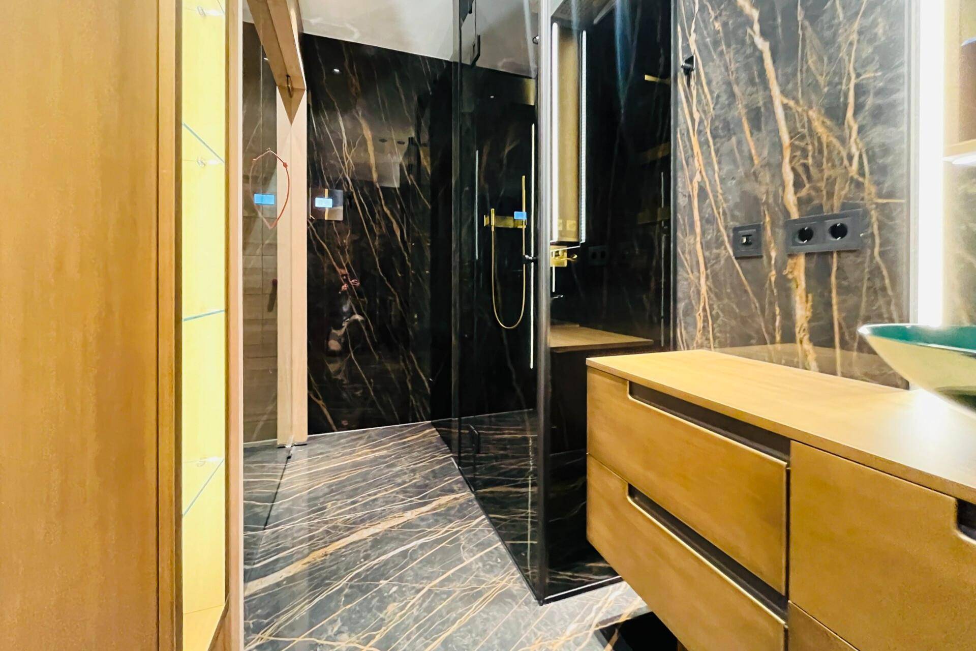 Elegantes Badezimmer mit dunklen Marmorwänden, Glasdusche und schwebendem Holzwaschtisch.