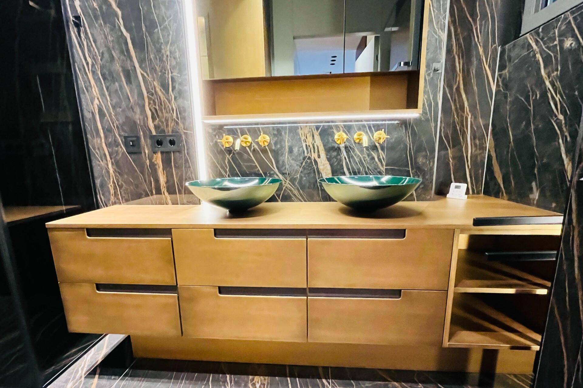 Moderner Waschtisch mit zwei grünen Aufsatzwaschbecken, goldenen Armaturen und Holzschränken.