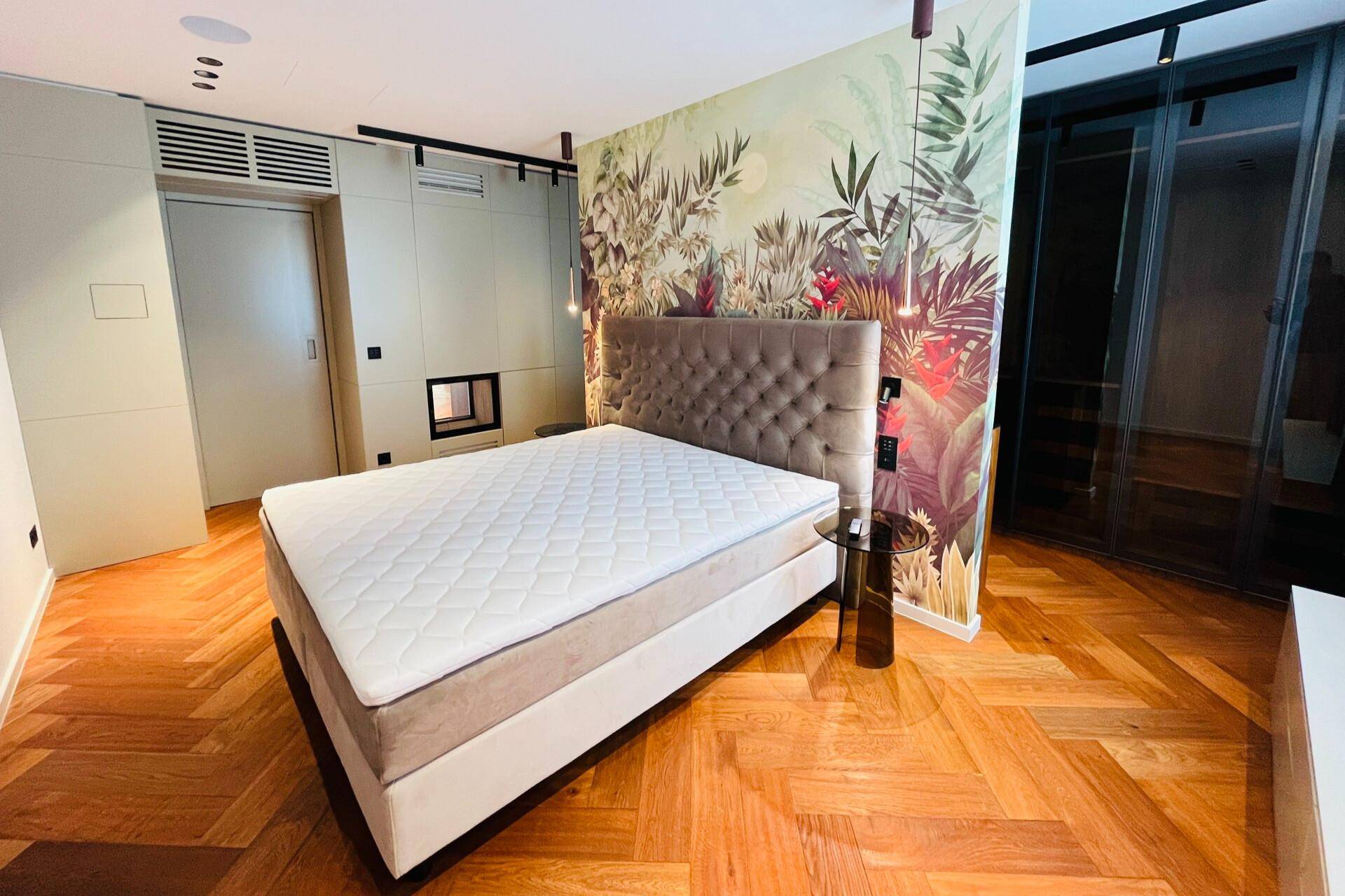 Schlafzimmer mit großem Bett, tropischer Akzentwand und elegantem Fischgrätparkettboden.