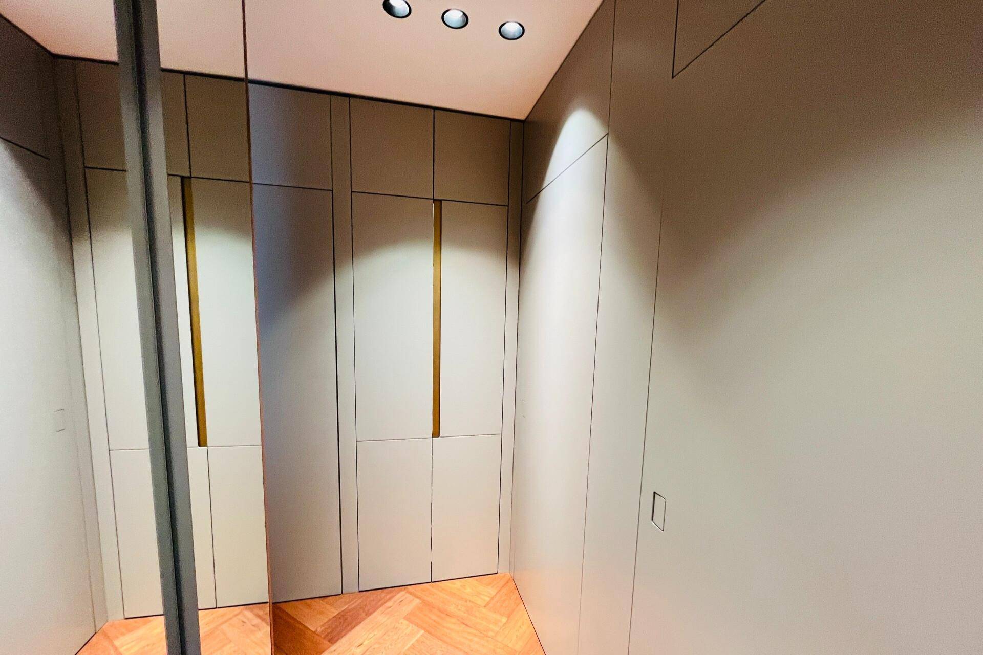 Begehbarer Kleiderschrank mit integrierten hellgrauen Schränken und einem großen Spiegel.