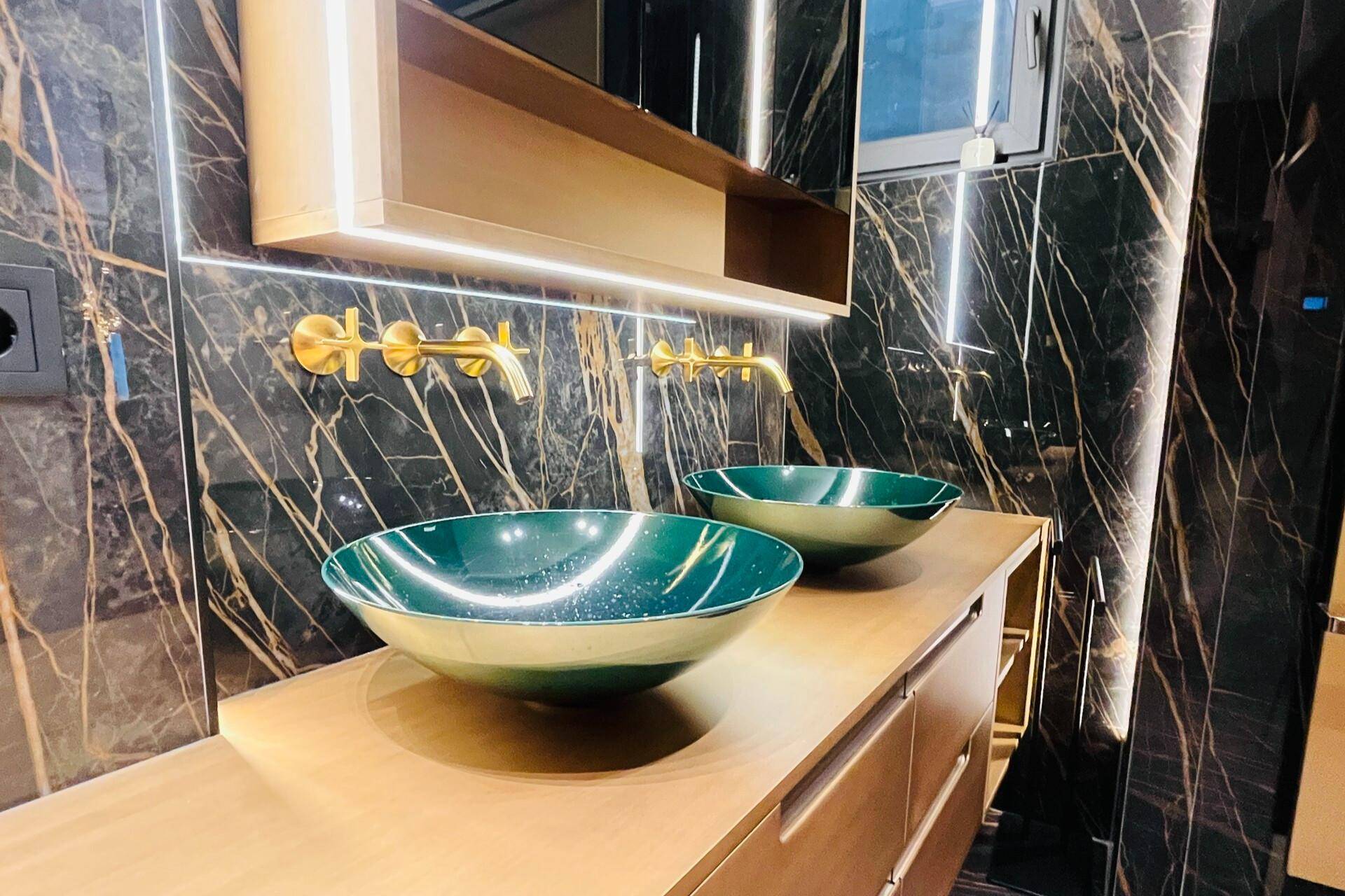 Modernes Badezimmer mit Doppelwaschbecken, grünen Aufsatzschalen und eleganten goldenen Armaturen.