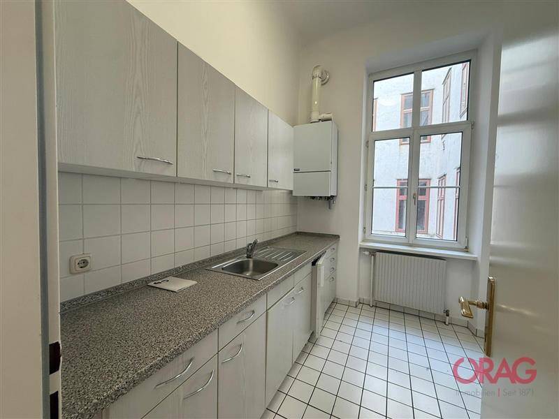 Funktionale Küche mit weißen Schränken, gefliestem Boden und Fensterblick.