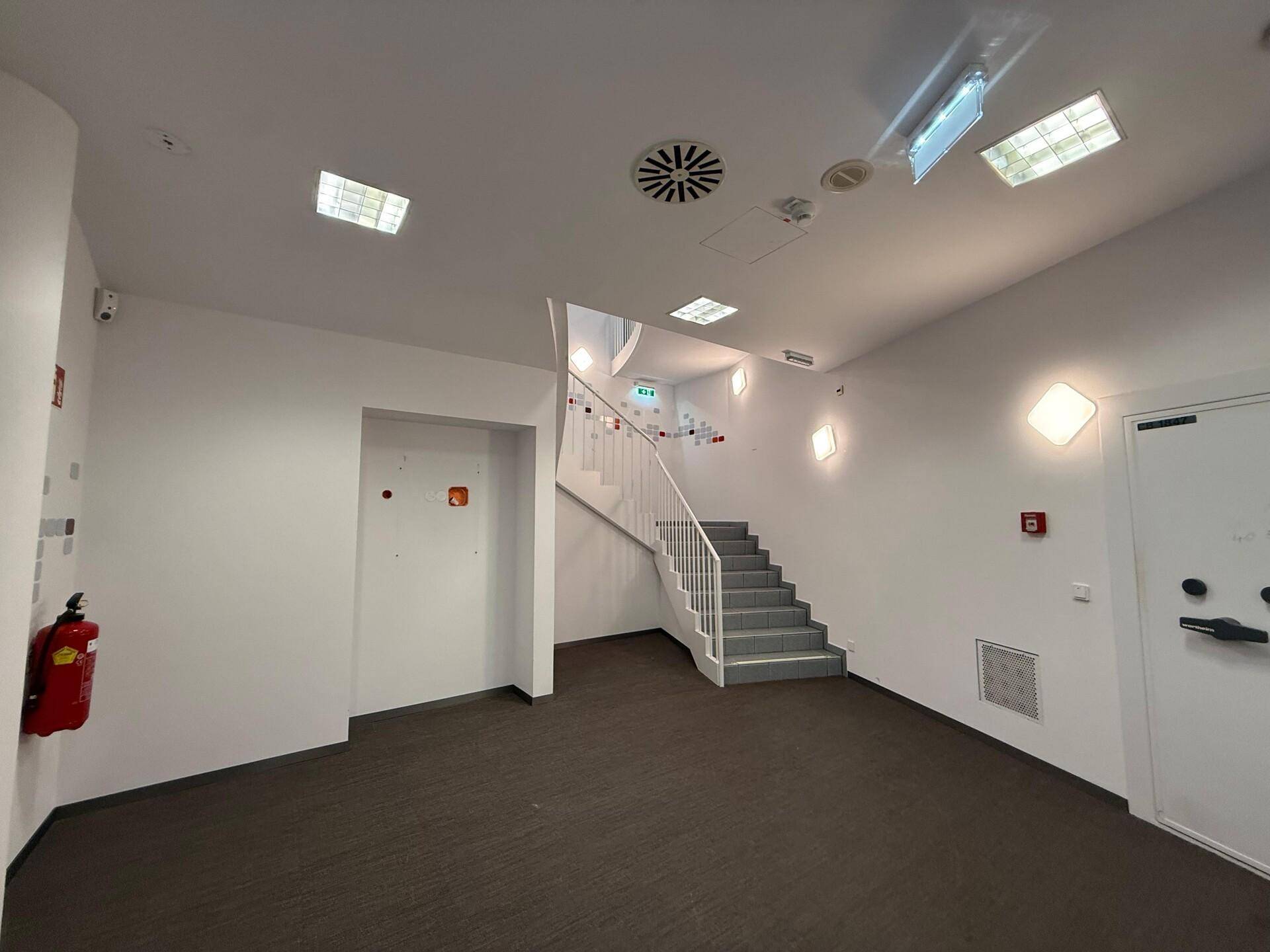 Heller Flurbereich mit Treppe, Teppichboden und weißen Wänden, ausgestattet mit Sicherheitskameras.