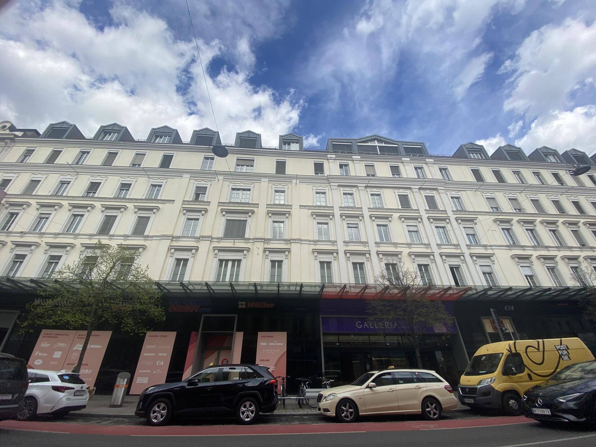 Historisches Gebäude mit klassischer Fassade und vielen Fenstern, darunter moderne Ladenfronten im Erdgeschoss.