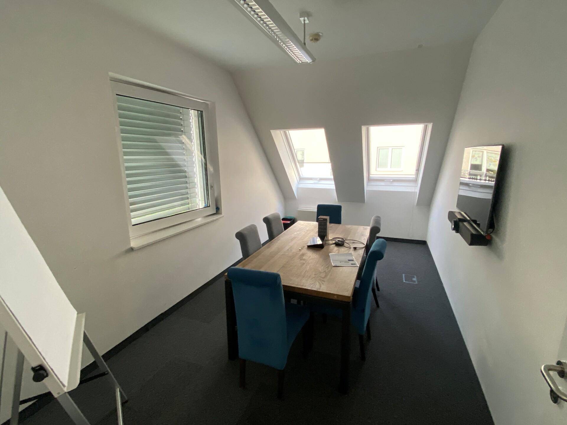 Besprechungsraum im Dachgeschoss mit schrägen Wänden, Dachfenstern und modernem Mobiliar.