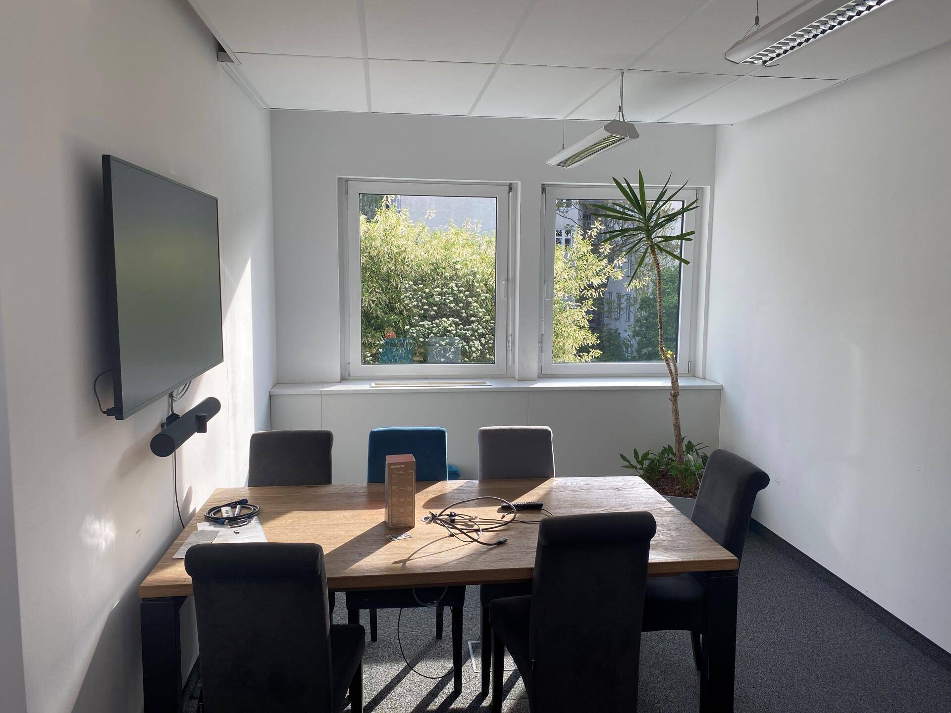 Moderner Konferenzraum mit großem Bildschirm, Holztisch und Blick ins Grüne.