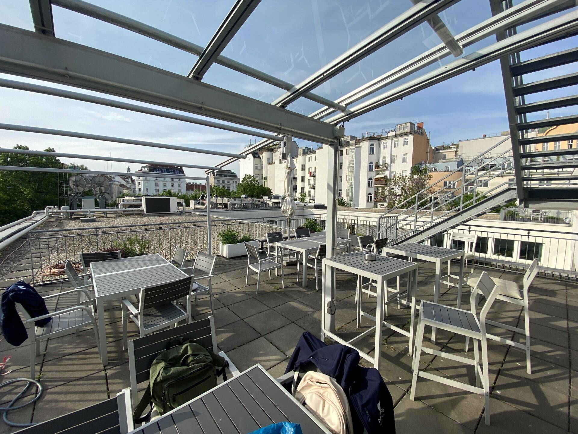 Geräumige Dachterrasse mit mehreren Sitzbereichen, Glasdach und Blick über die Stadt.