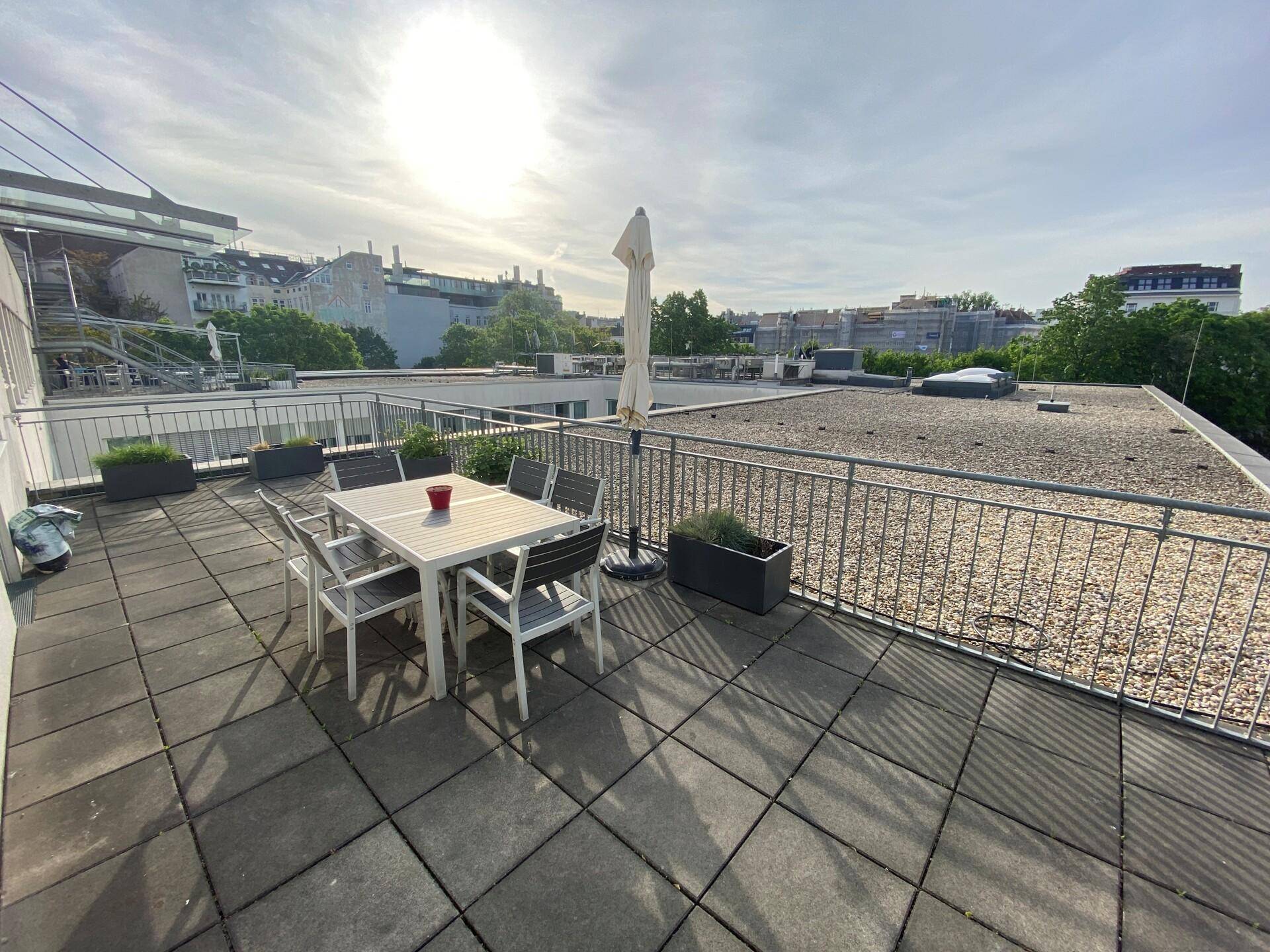 Sonnige Dachterrasse mit Esstisch, Stühlen und Sonnenschirm, ideal für entspannte Stunden im Freien.