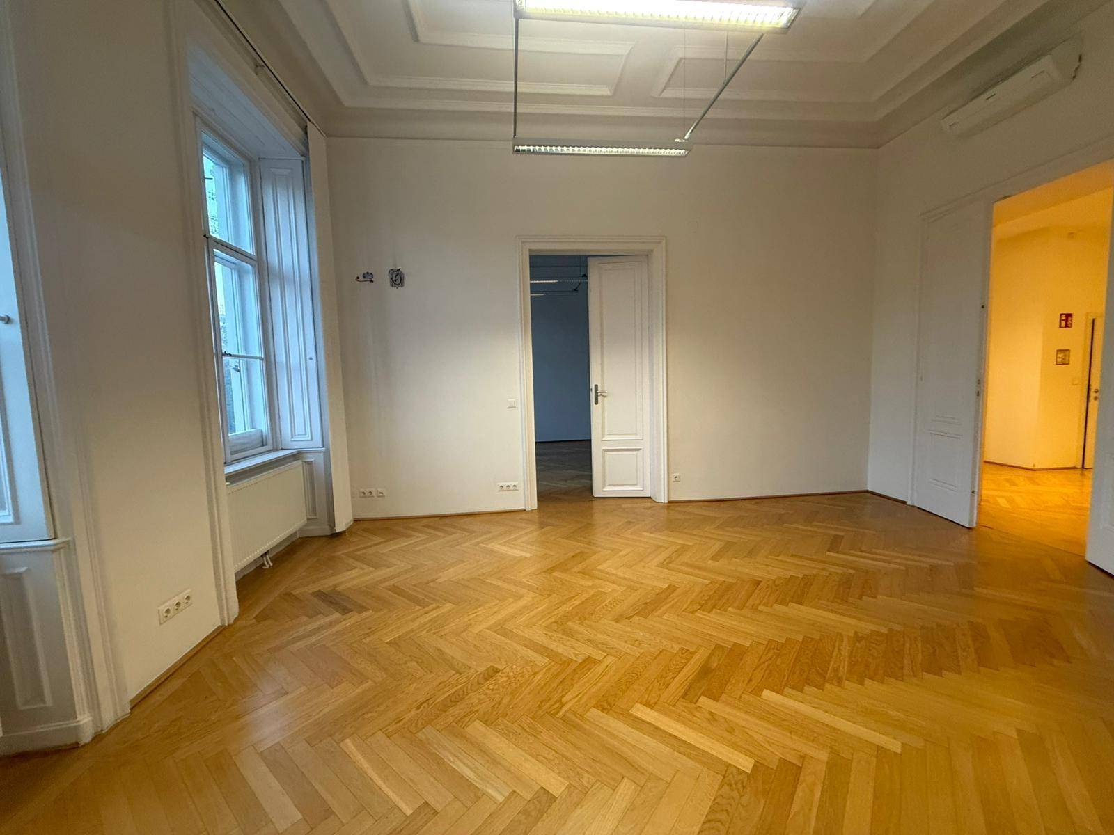 Geräumiger Wohnbereich mit Fischgrätparkett, hohen Decken und Zugang zu weiteren Räumen.