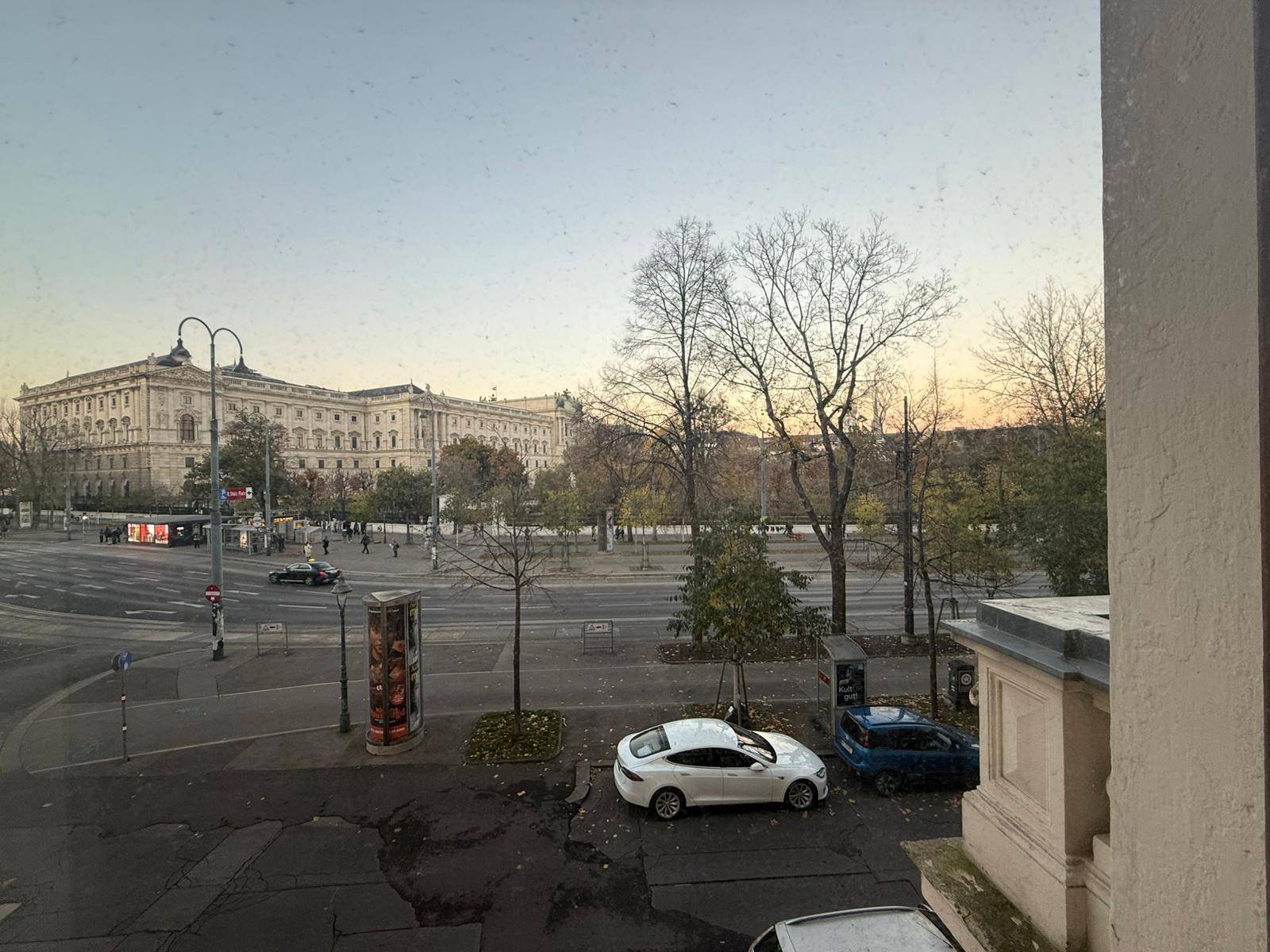 Blick aus dem Fenster auf eine belebte Straße und ein historisches Gebäude in der Ferne.