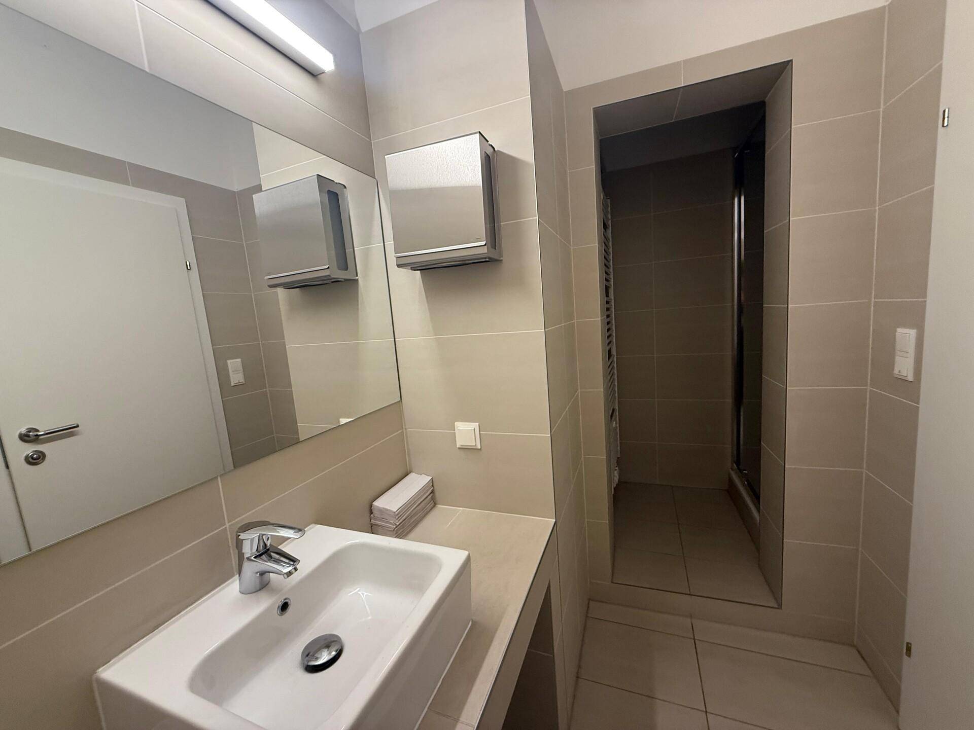 Modernes Badezimmer mit beigefarbenen Fliesen, Waschbecken und einer begehbaren Dusche.