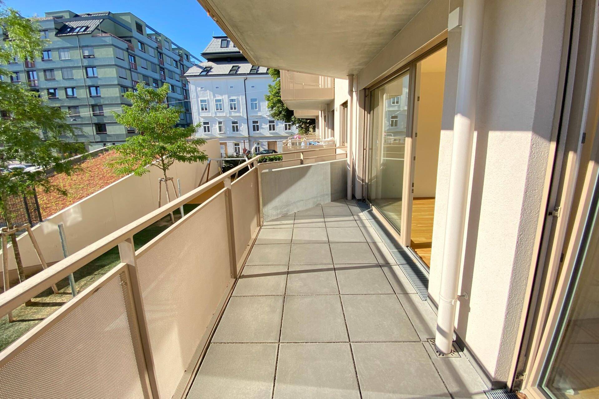 Heller Balkon mit grauen Fliesen und Blick auf die umliegenden Gebäude und Bäume.