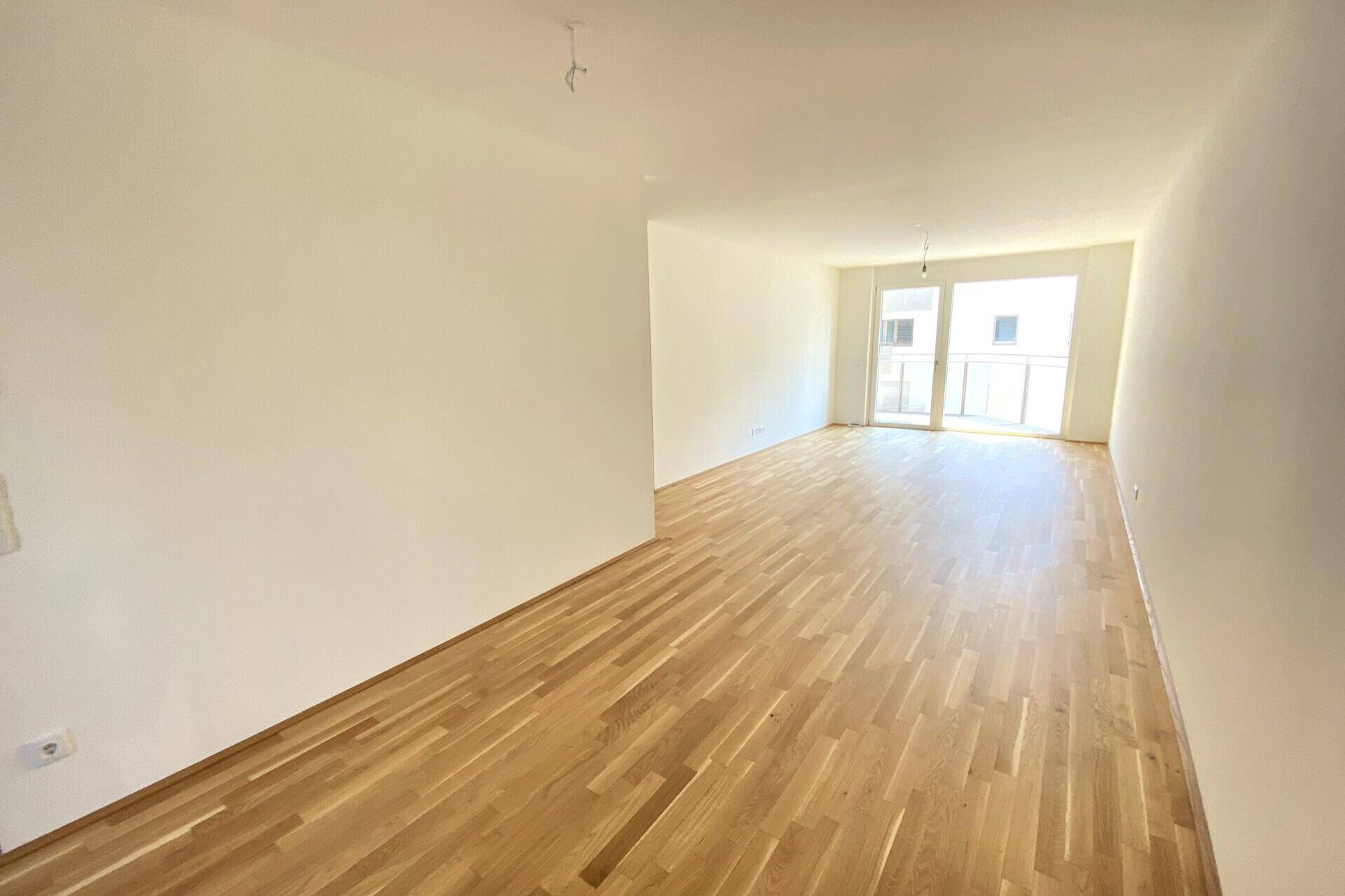 Geräumiges, leeres Wohnzimmer mit hellem Holzboden und viel Tageslicht.