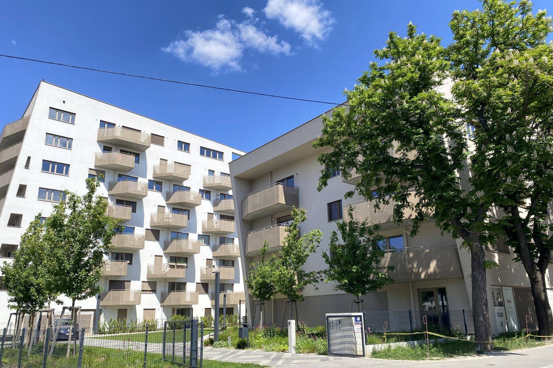 Zwei moderne Wohngebäude mit Balkonen und grüner Umgebung an einem sonnigen Tag.