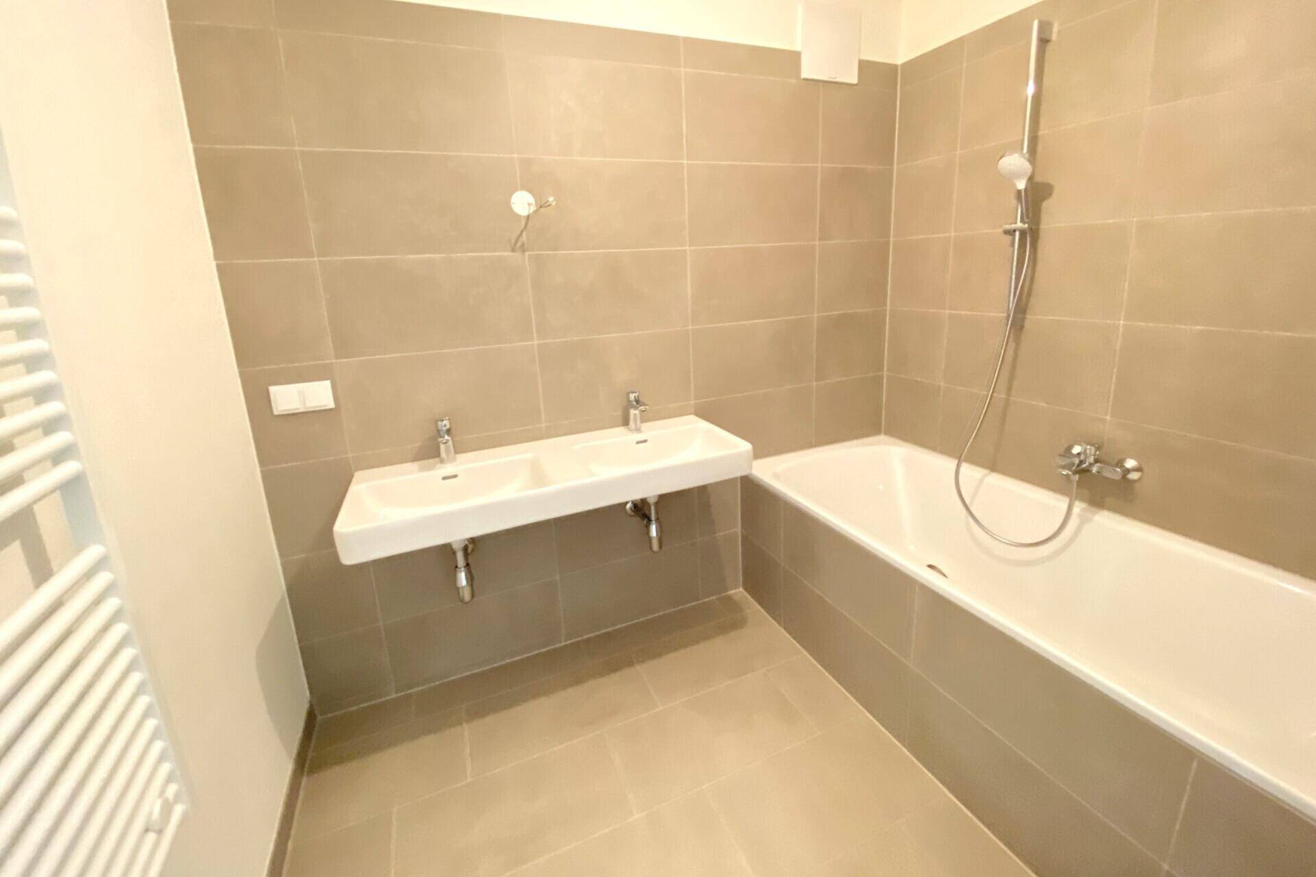 Modernes Badezimmer mit Doppelwaschbecken, Badewanne und beigefarbenen Fliesen.