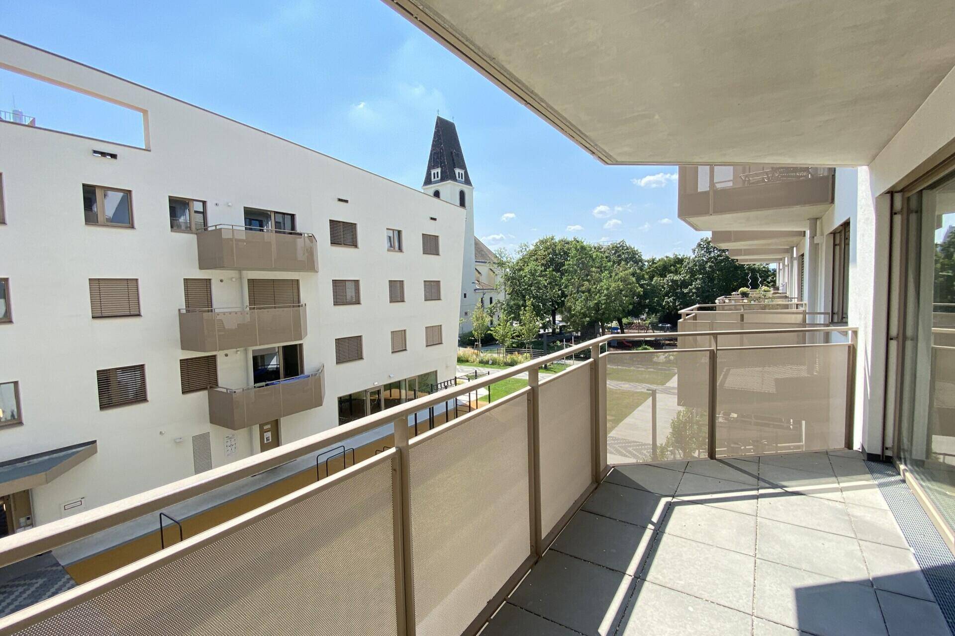 Geräumiger Balkon mit Fliesenboden und Blick auf die umliegenden Gebäude und einen Kirchturm.