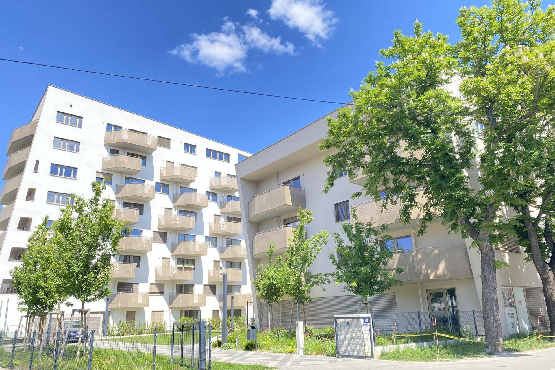 Moderne Wohngebäude mit Balkonen und grüner Umgebung unter strahlend blauem Himmel.