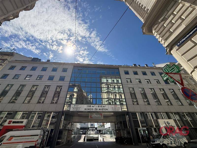 Weitwinkelaufnahme eines modernen Bürogebäudes mit Glasfassade und Werbebanner an einer belebten Straße.