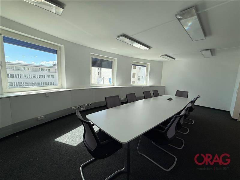 Geräumiger Konferenzraum mit langem Tisch und Stühlen, Teppichboden und mehreren Fenstern für Tageslicht.