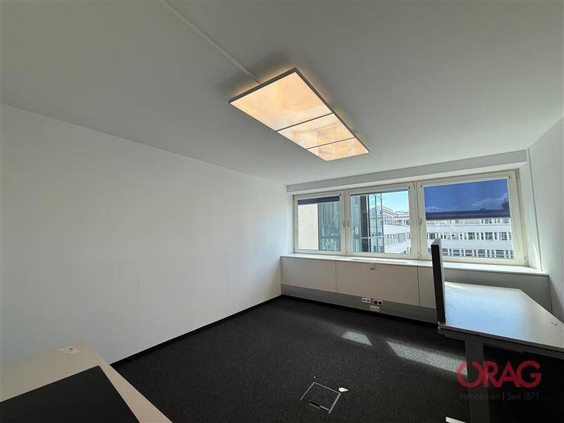 Helles Einzelbüro mit Teppichboden, großen Fenstern und moderner Deckenbeleuchtung, ideal für konzentriertes Arbeiten.
