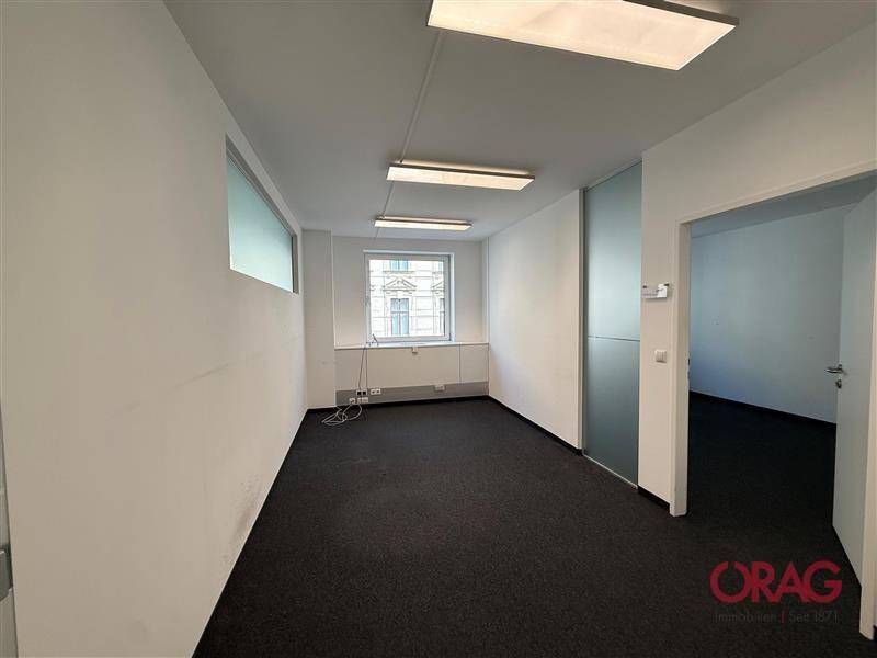 Leeres Büro mit Teppichboden, weißen Wänden und einem Fenster, das Tageslicht hereinlässt, bereit zur Einrichtung.