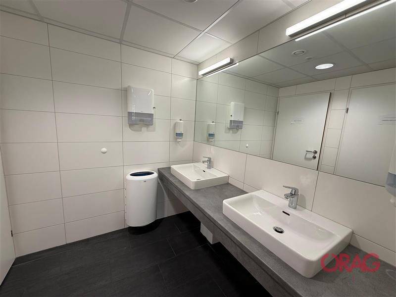 Modernes Badezimmer mit zwei Waschbecken, großem Spiegel und weißen Fliesen, ausgestattet für mehrere Nutzer.