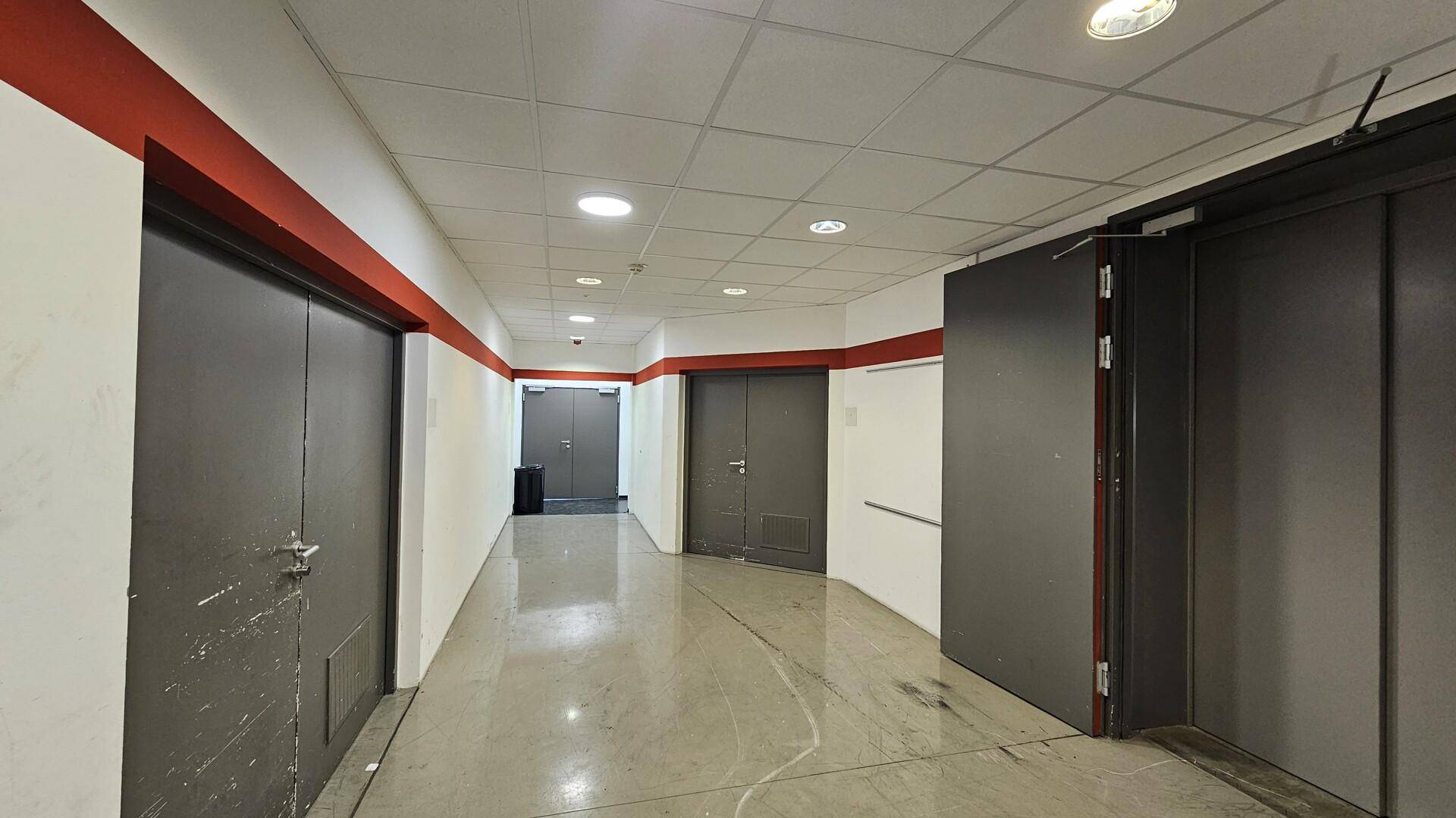 Langer Flur mit mehreren Türen, abgehängter Decke und einem roten Streifen an der Wand.