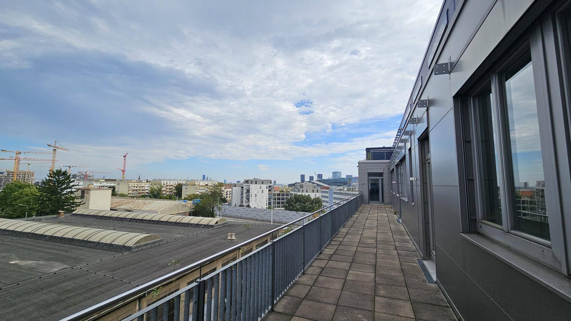 Lange Außenterrasse im Obergeschoss mit Metallgeländer und Panoramablick über die Stadt.