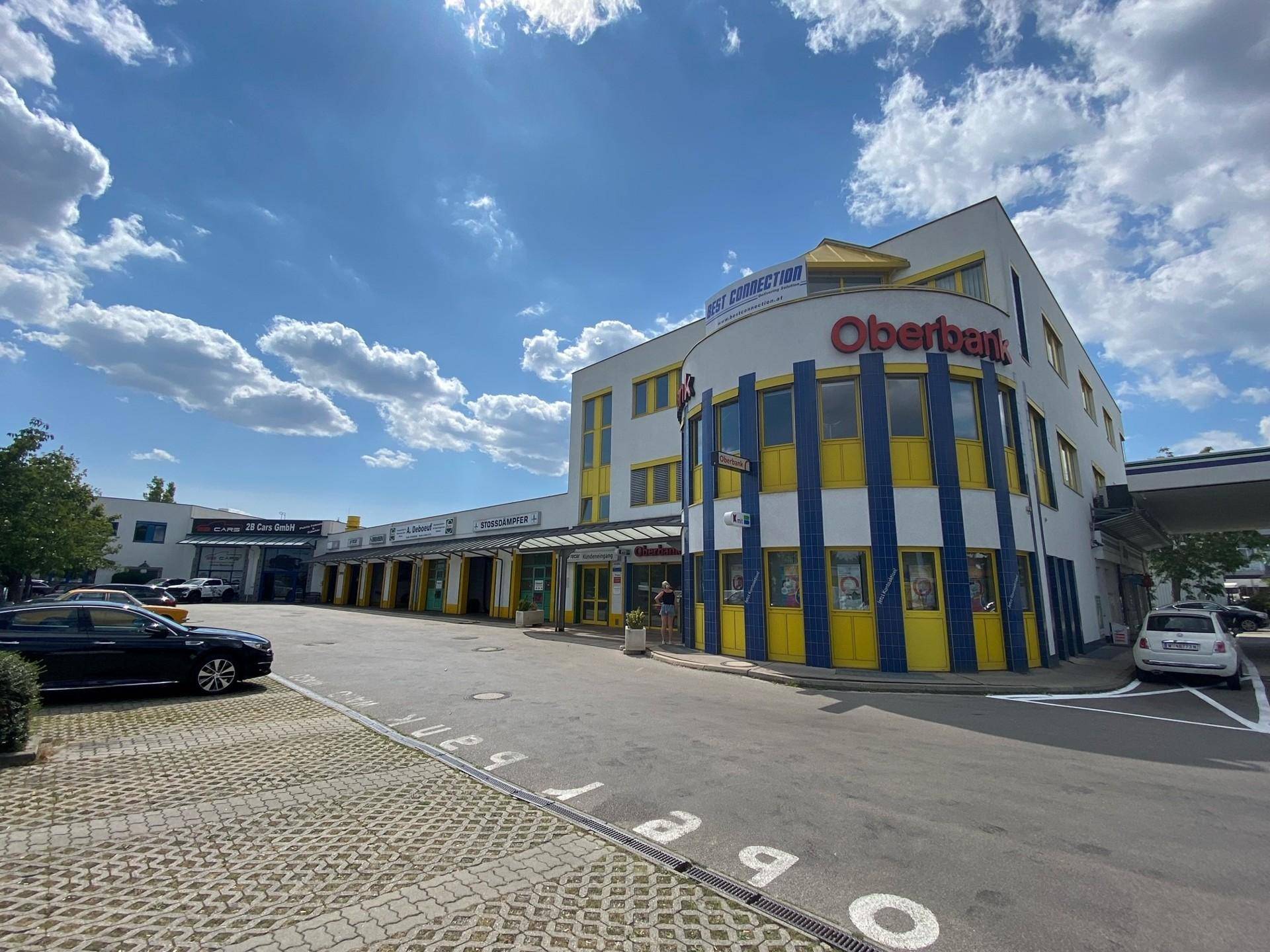 Außenansicht eines modernen Geschäftsgebäudes mit Oberbank-Filiale und einem großen Parkplatz davor.