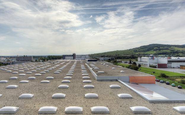 Dachansicht eines großen Industriegebäudes mit zahlreichen Oberlichtern, umgeben von grünen Hügeln.