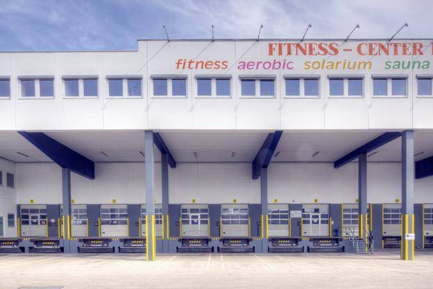 Gewerbegebäude mit mehreren Laderampen und einem großen Schriftzug für ein Fitnesscenter an der Fassade.