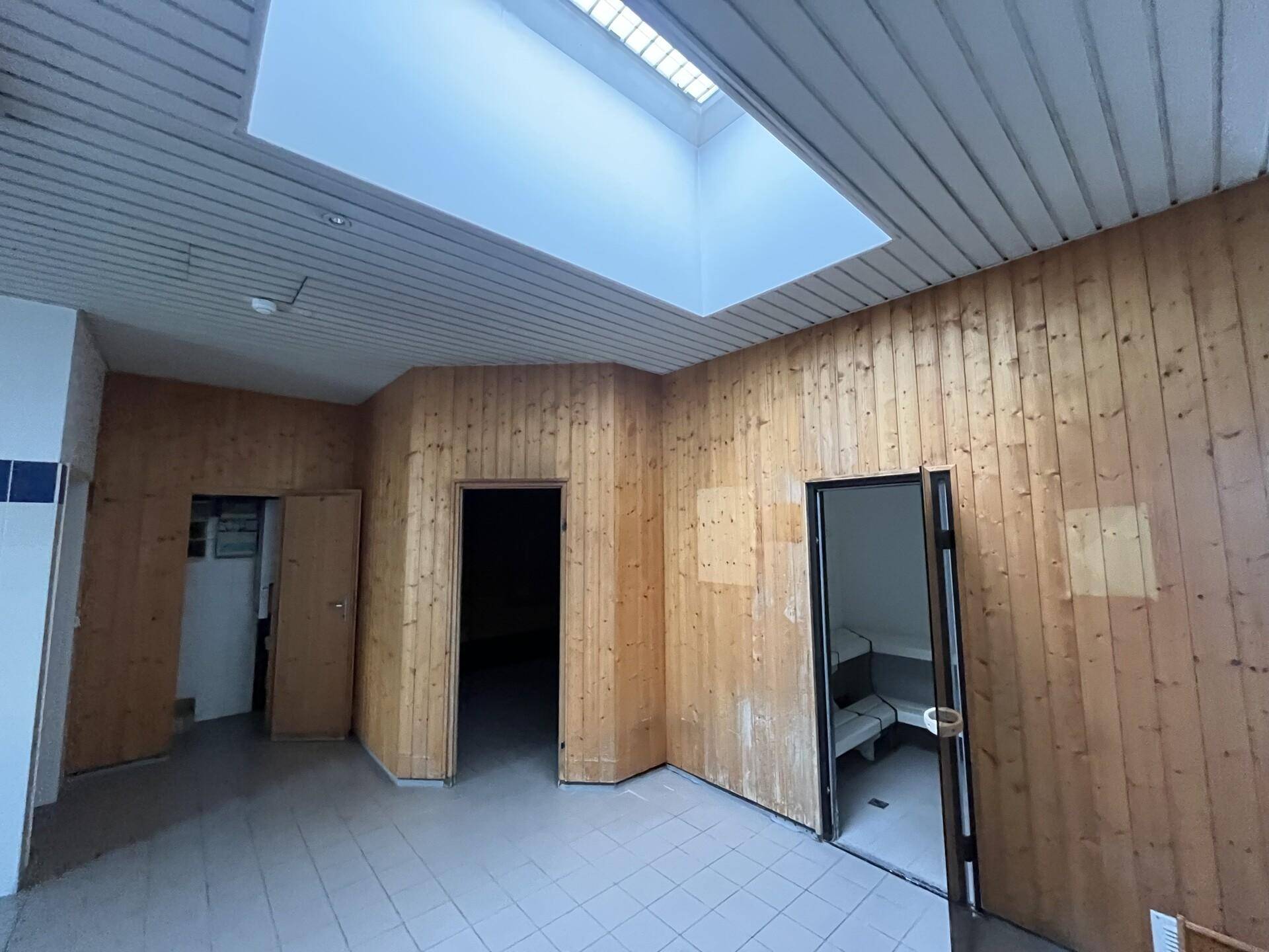 Raum mit Holzverkleidung, Fliesenboden und großem Oberlicht, möglicherweise ein Umkleide- oder Saunabereich.
