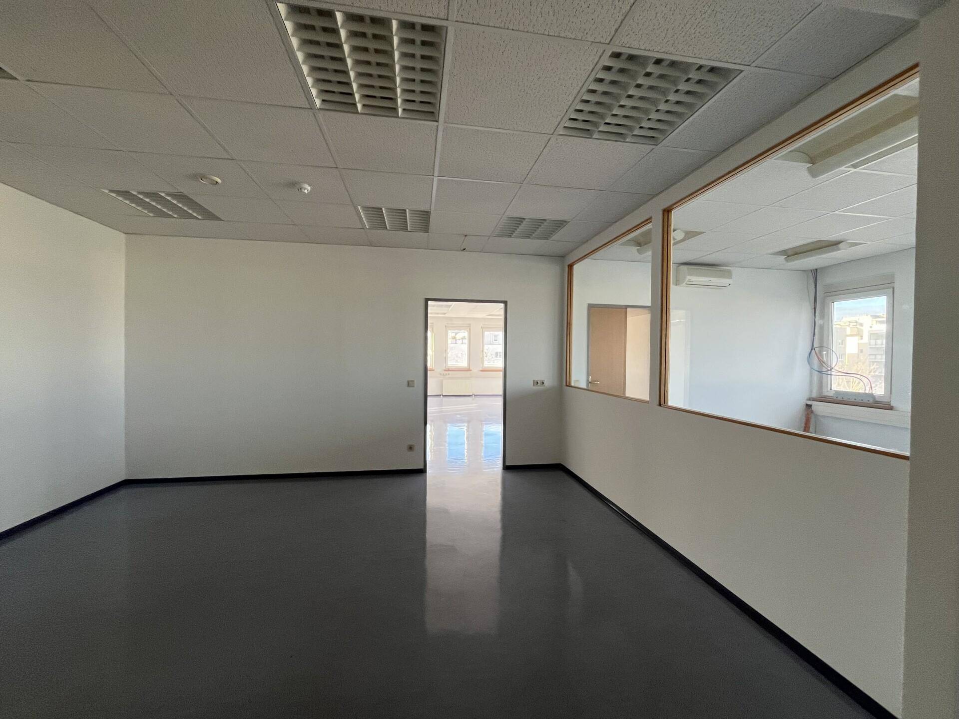 Geräumiges, leeres Büro mit offenem Durchgang und einer Glaswand zu einem weiteren Bereich.