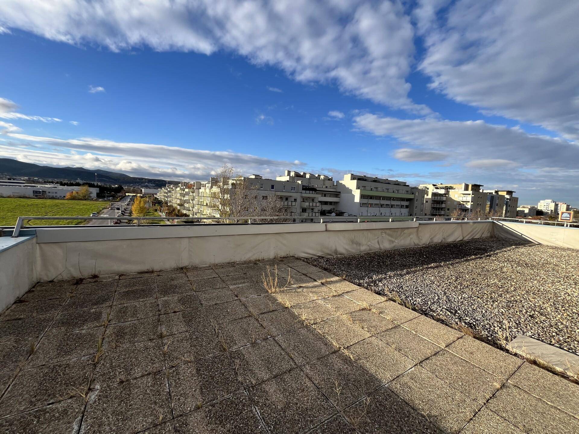 Große Dachterrasse mit Fliesen und Kies, bietet einen weiten Blick auf die umliegende Bebauung und Grünflächen.