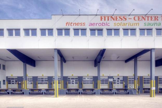 Fassade eines Gewerbegebäudes mit mehreren Laderampen und Beschriftung für ein Fitnesscenter.