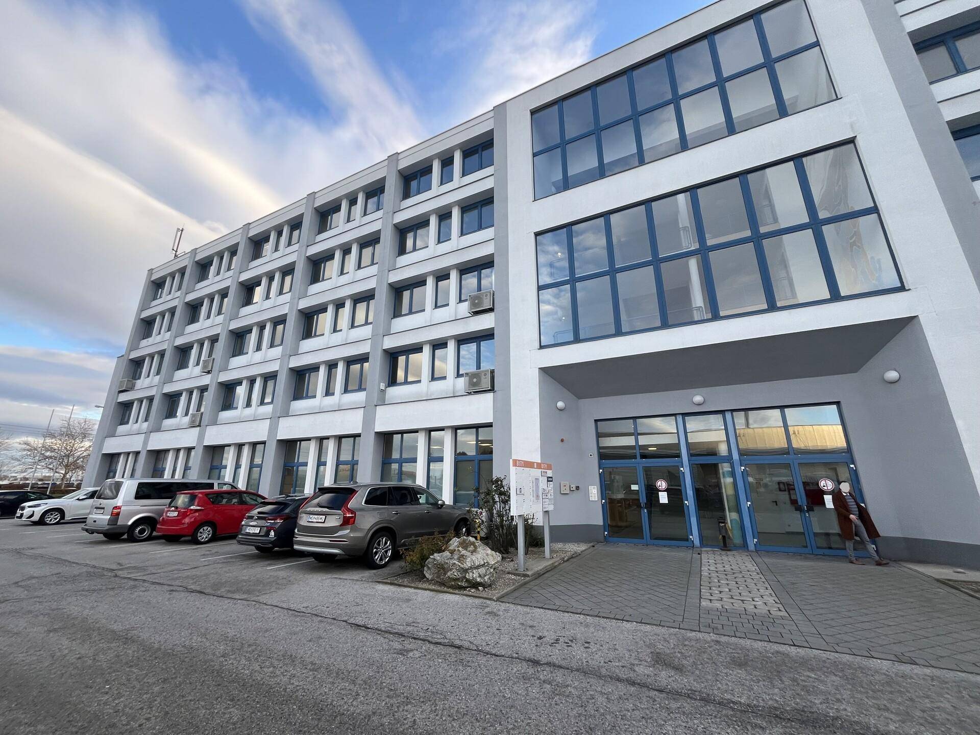 Außenansicht des mehrstöckigen Bürogebäudes mit großen Fenstern und einem Parkplatz davor.