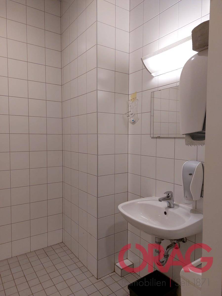 Kleines Badezimmer mit weißen Fliesen an Wänden und Boden, ausgestattet mit Waschbecken und Spiegel.