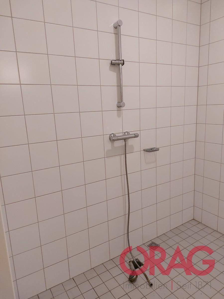 Duschbereich mit weißen Wand- und Bodenfliesen, ausgestattet mit einer einfachen Duscharmatur.