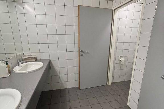 Einfacher Toilettenraum mit weißen Fliesen, zwei Waschbecken und grauen Bodenfliesen, sauber und funktional.