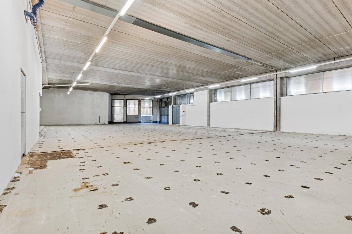 Geräumiger Gewerberaum mit Betonboden, hohen Decken und großen Fenster- und Türbereichen.