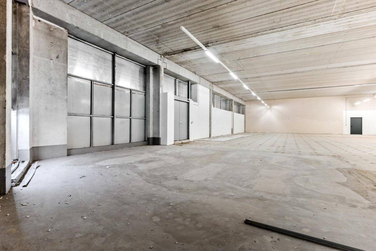 Heller Gewerberaum mit Betonboden und großen Fensterfronten, die viel Tageslicht hereinlassen.